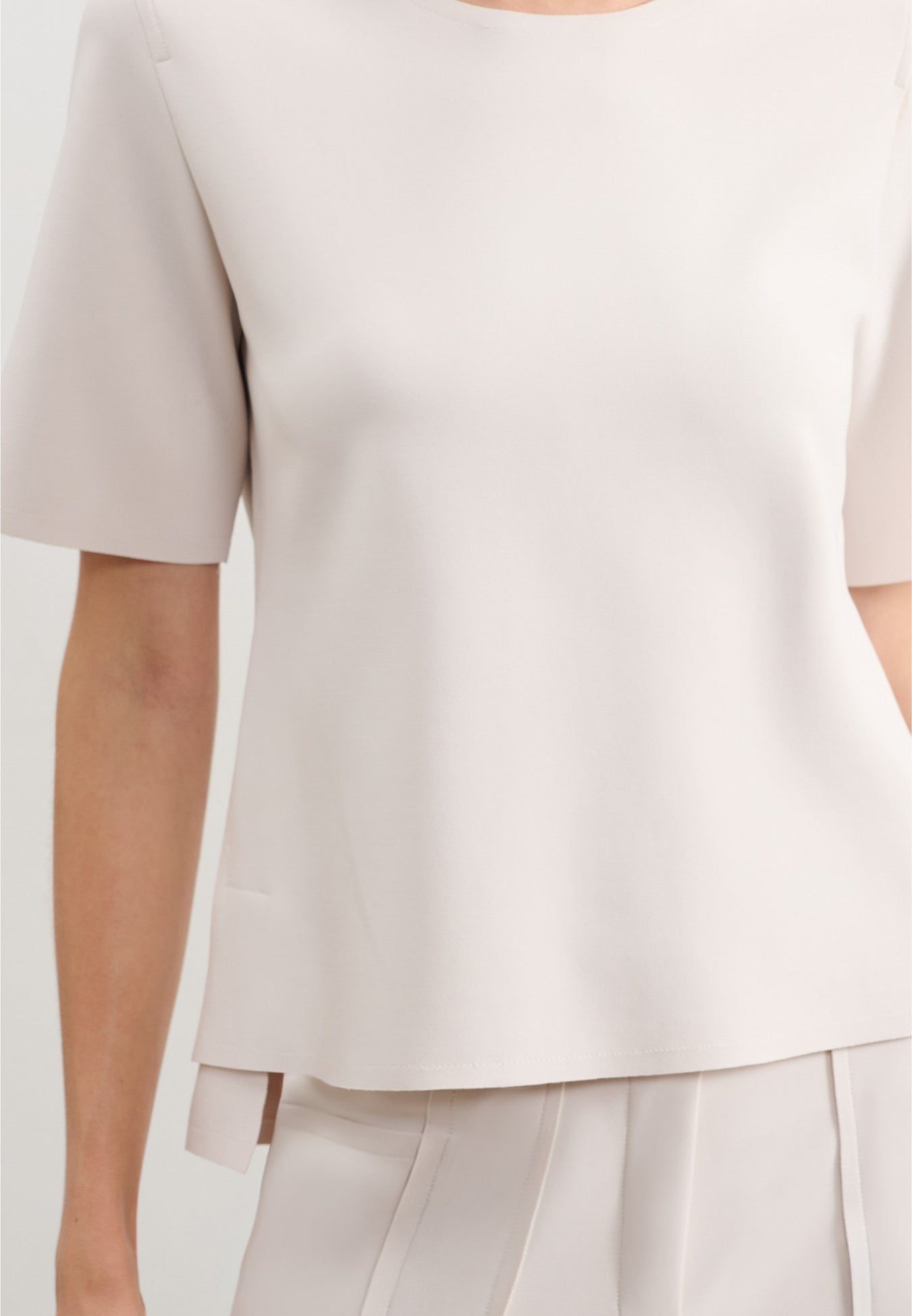 Modelo veste uma blusa branca de decote arredondado e mangas curtas, combinada com uma calça da mesma cor.