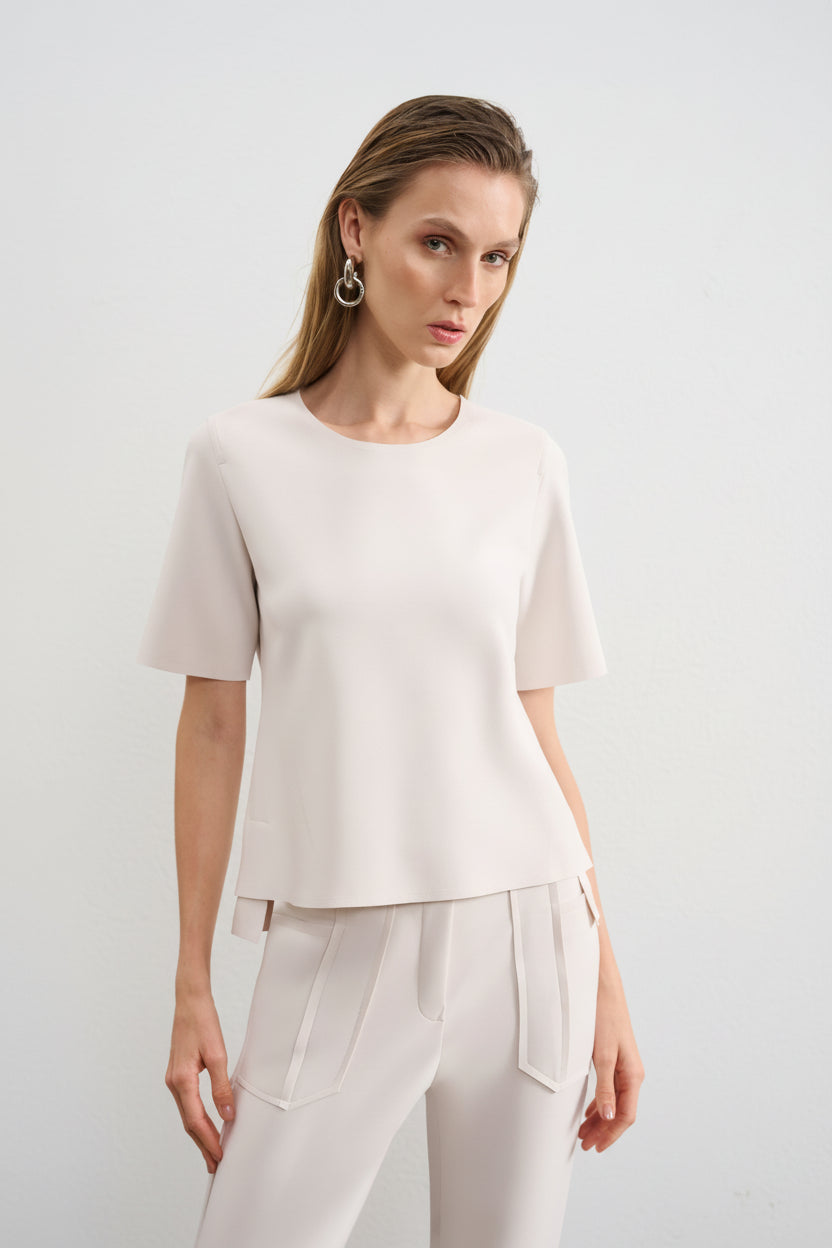 Modelo veste uma blusa branca de decote arredondado e mangas curtas, combinada com uma calça da mesma cor.