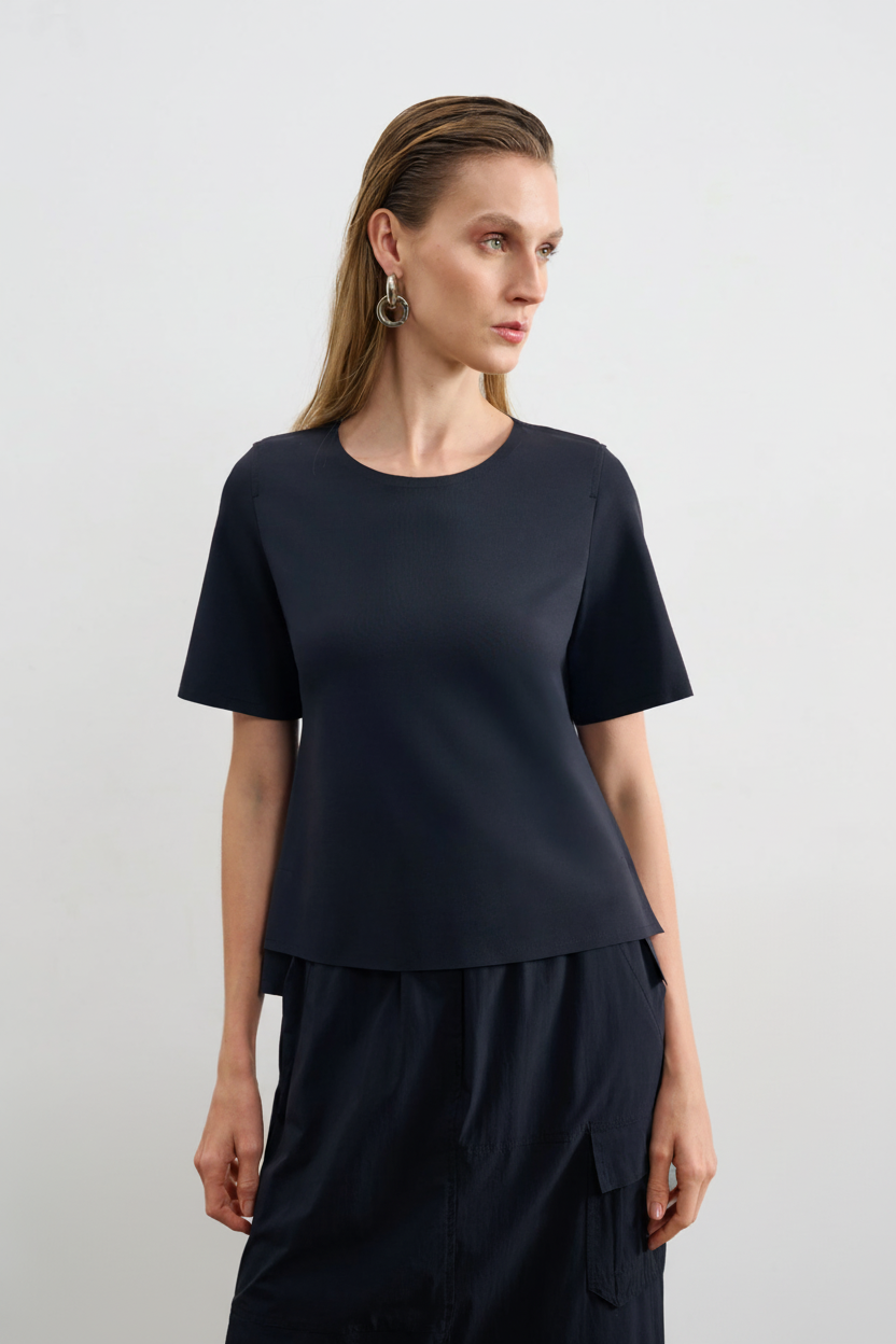 Modelo veste uma blusa preta de decote arredondado e mangas curtas, combinada com uma saia preta com bolsos cargô.