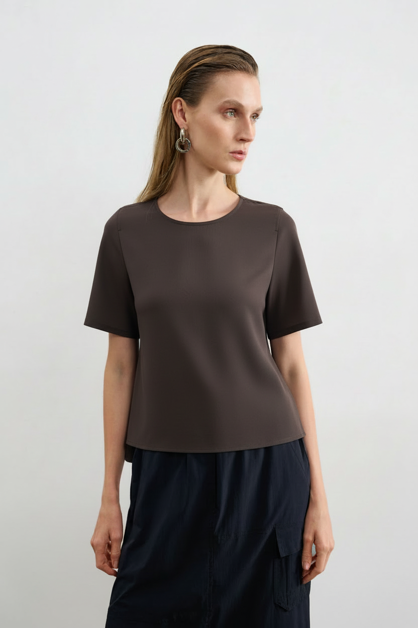 Modelo veste uma blusa marrom de decote arredondado e mangas curtas, combinada com uma saia preta com bolsos cargô.