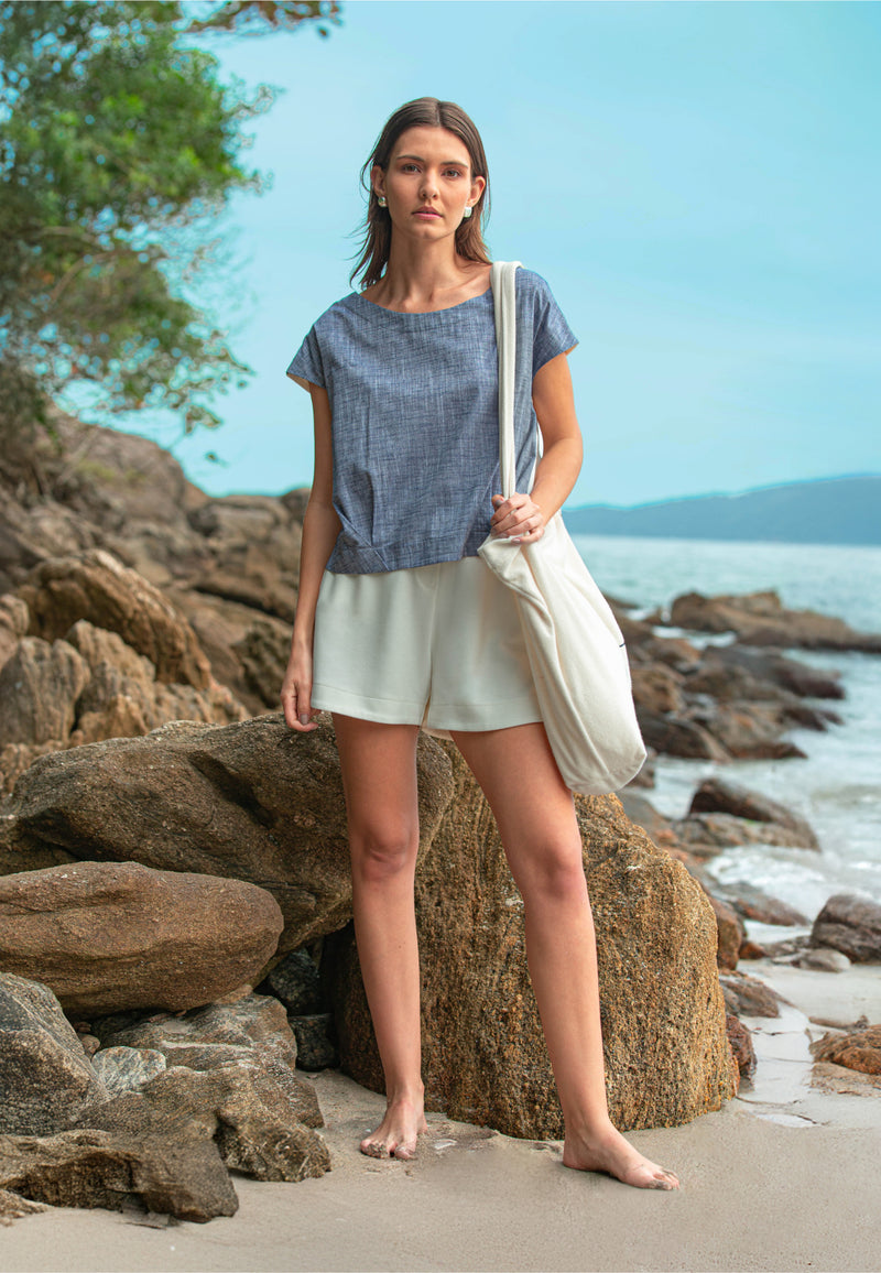 Modelo usando uma blusa marinho mescla de mangas curtas, shorts brancos e uma bolsa de ombro volumosa em tom off-white.