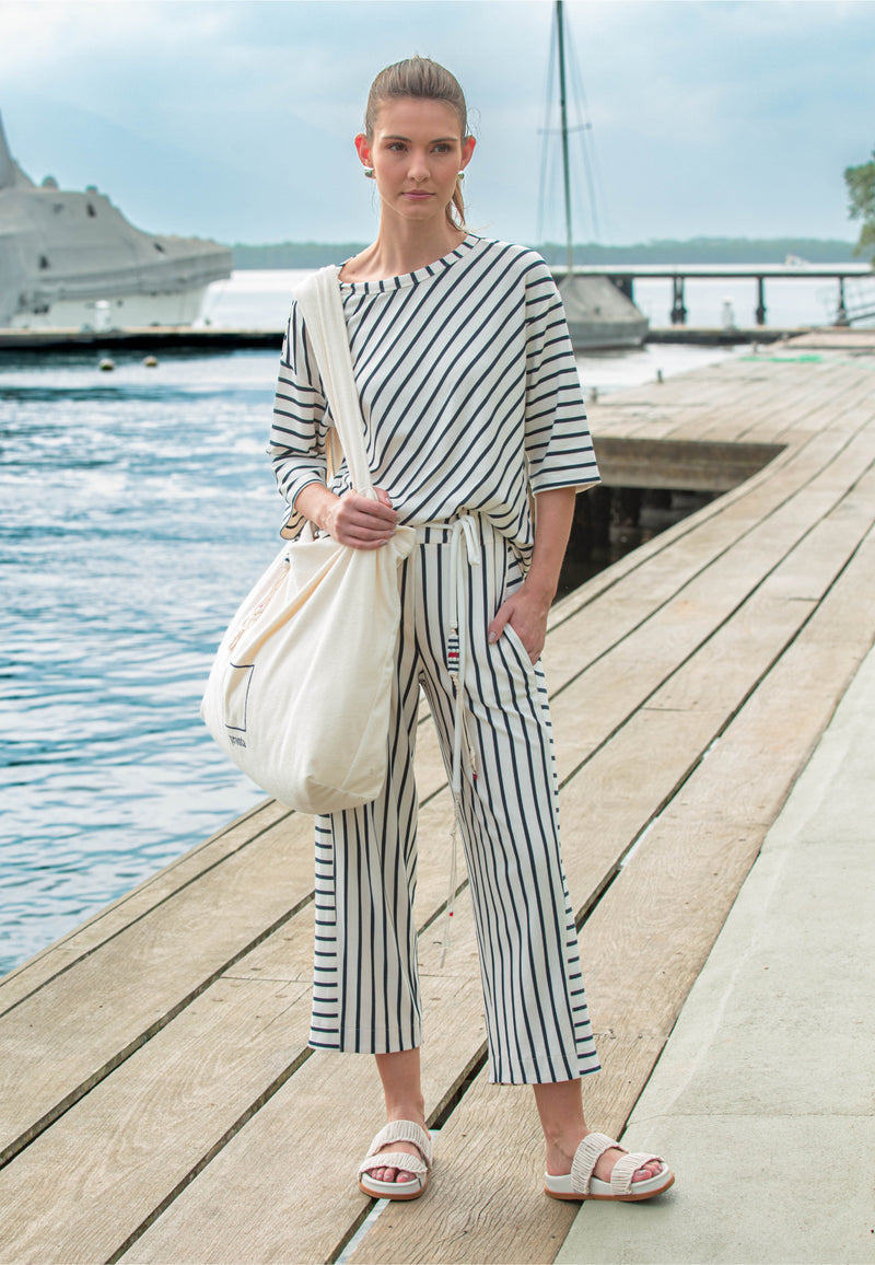 Modelo com conjunto casual composto por uma blusa e calça com listras diagonais e horizontais em azul marinho com cordão decorativo. 