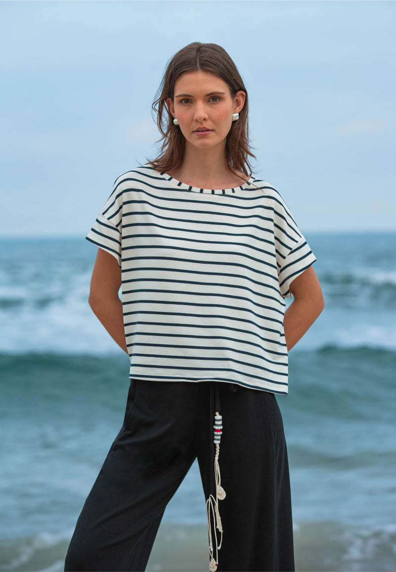 Modelo com conjunto casual composto por uma blusa com listras horizontais em azul marinho e calça preta.