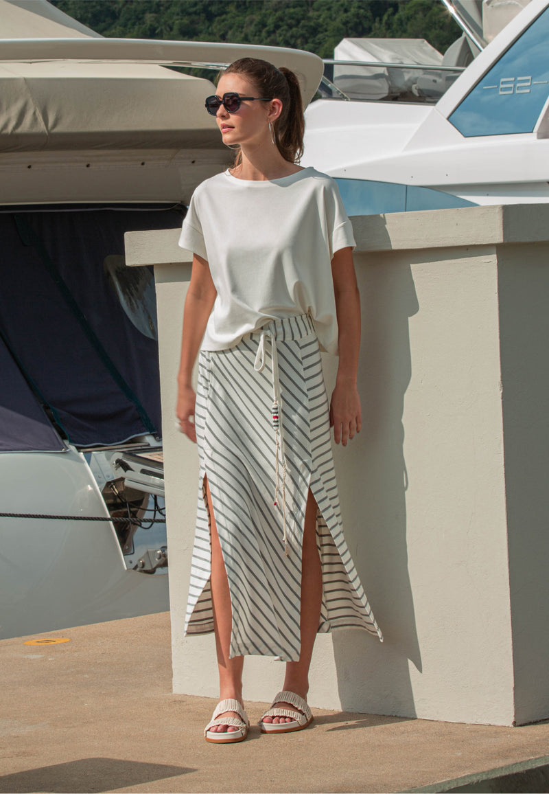 Modelo com conjunto casual composto por uma blusa branca de manga curta e saia midi com fendas nas laterais e listras cinza.