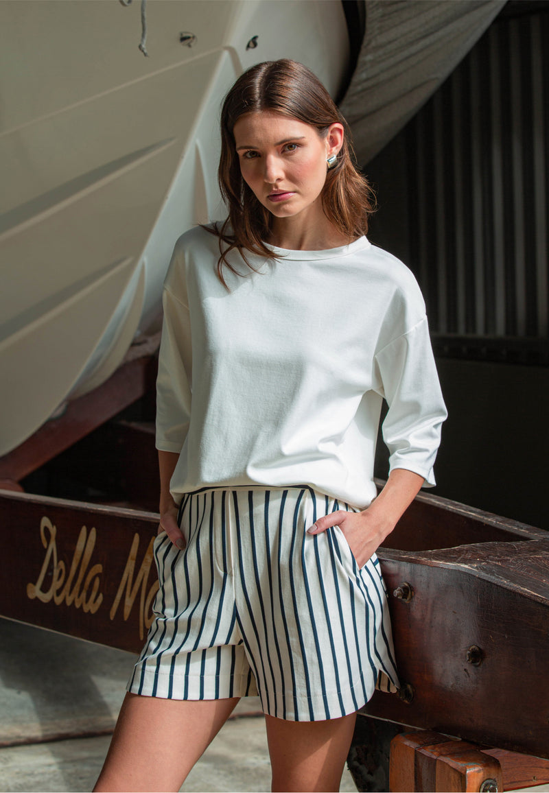 Modelo com conjunto casual composto por uma blusa branca de mangas 3/4 e shorts de cintura alta com listras verticais em azul marinho.