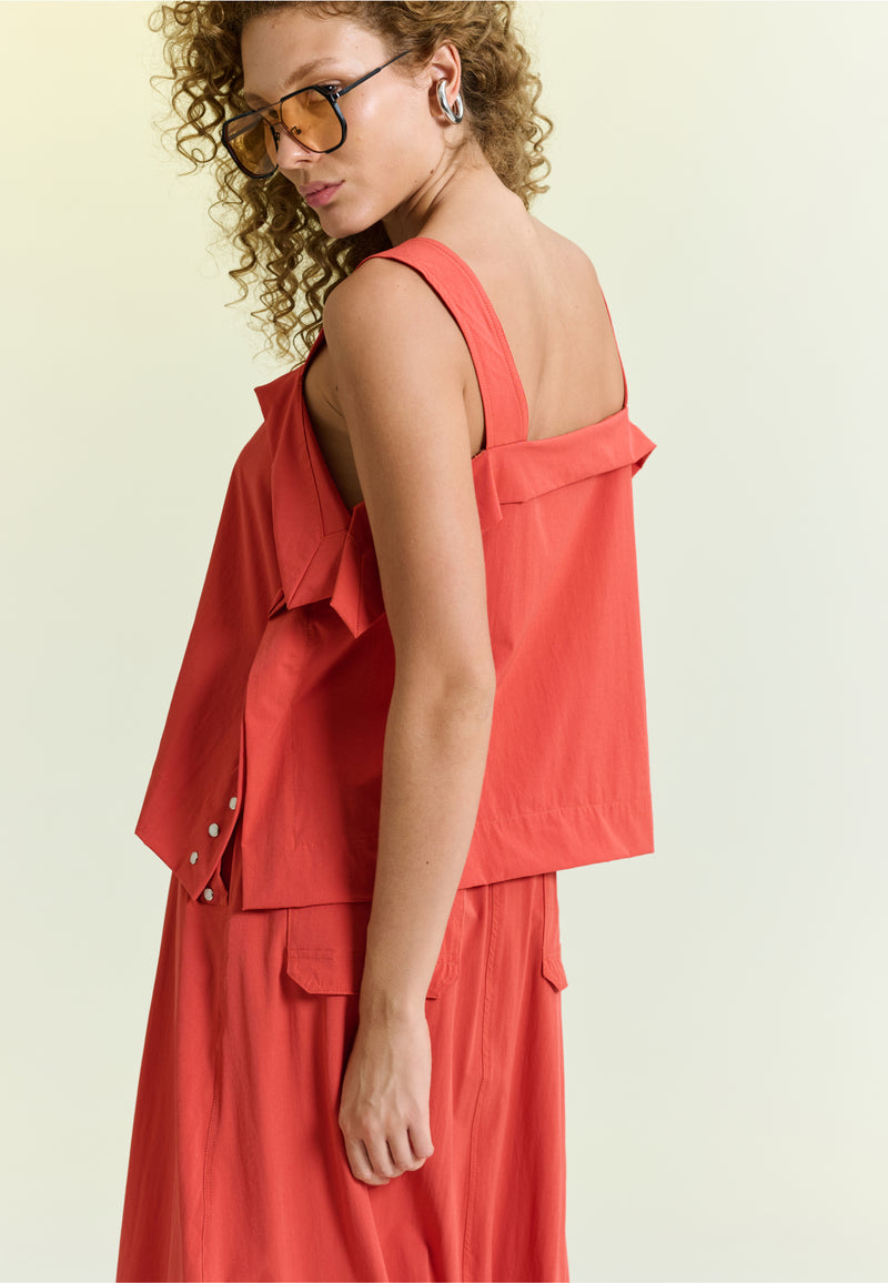 Modelo de costas exibe blusa com alças largas e sobreposição no decote.