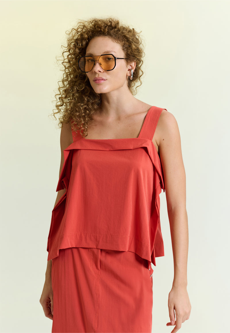 Modelo veste uma blusa terracota com alças largas e detalhe de sobreposição estruturada no decote.