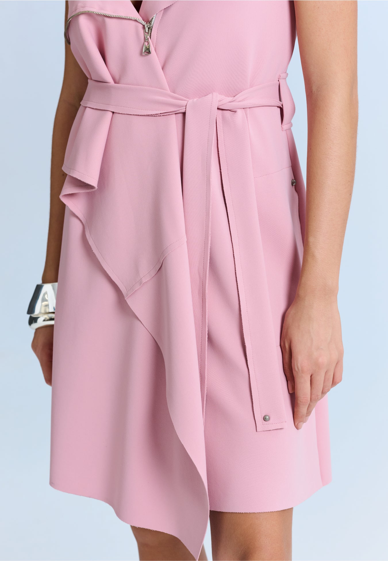 Modelo com um vestido curto rosa de decote em V com sobreposição frontal assimétrica.