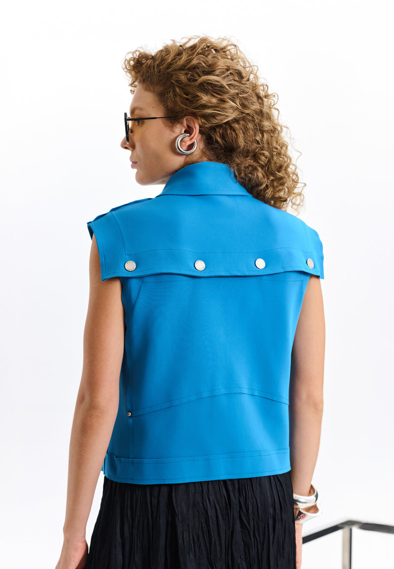 Modelo de costas usando um colete estruturado azul com lapela posterior ampla adornada por botões metálicos circulares.