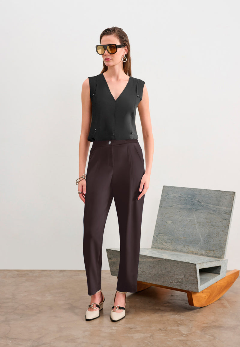 Modelo usando uma regata preta de decote em V, calças de alfaiataria marrom-escuro e sapatos de bico fino.