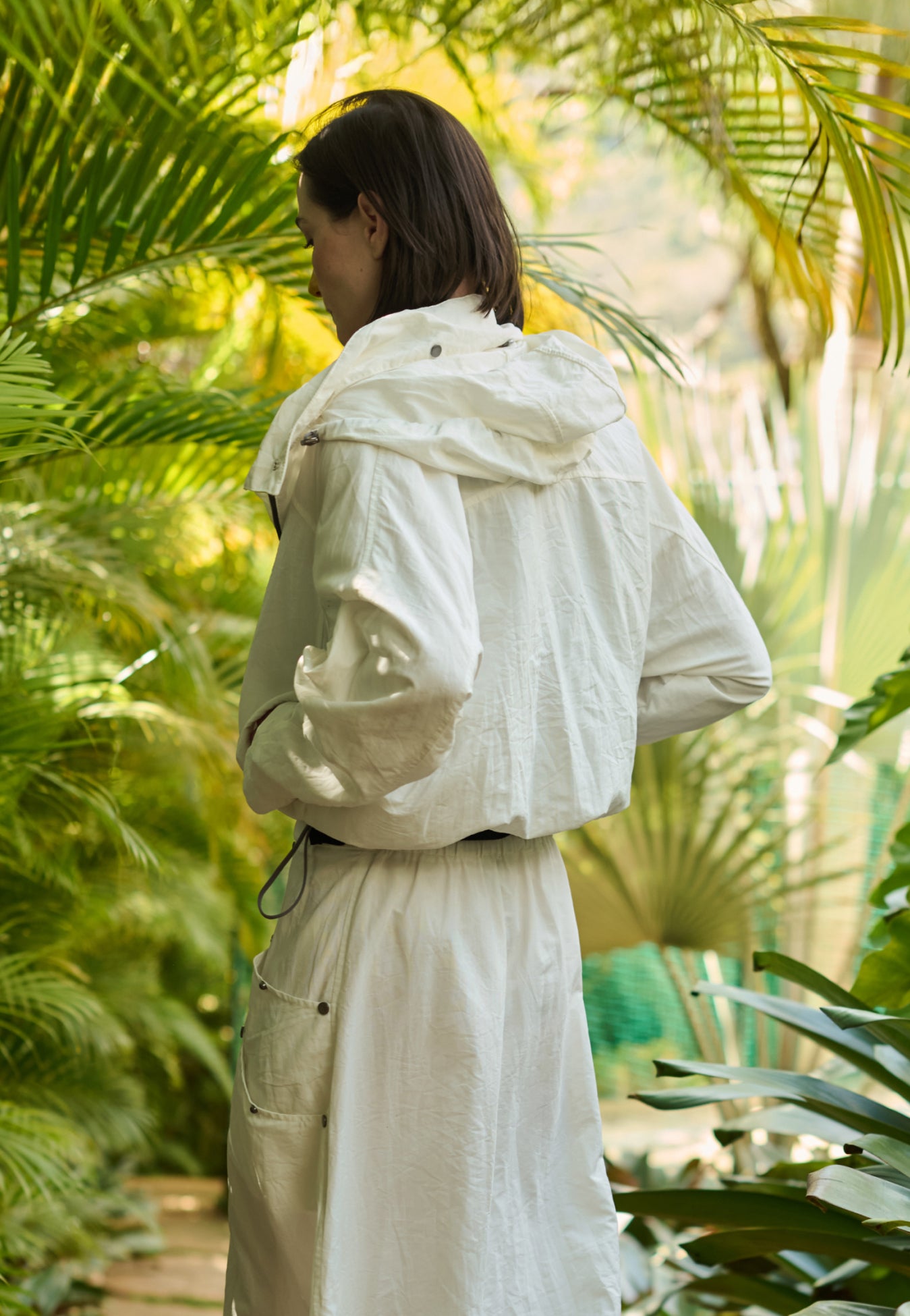 Modelo de costas veste uma jaqueta off-white com capuz, combinada com uma saia midi off-white que possui bolsos laterais utilitários com rebites.