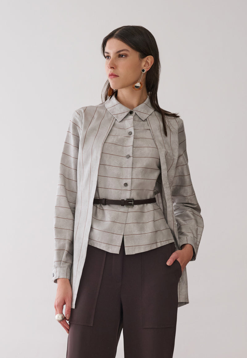 Modelo veste uma camisa com sobreposição integrada cinza com listras marrons, combinada com calças marrons de bolsos utilitários e cinto fino. 