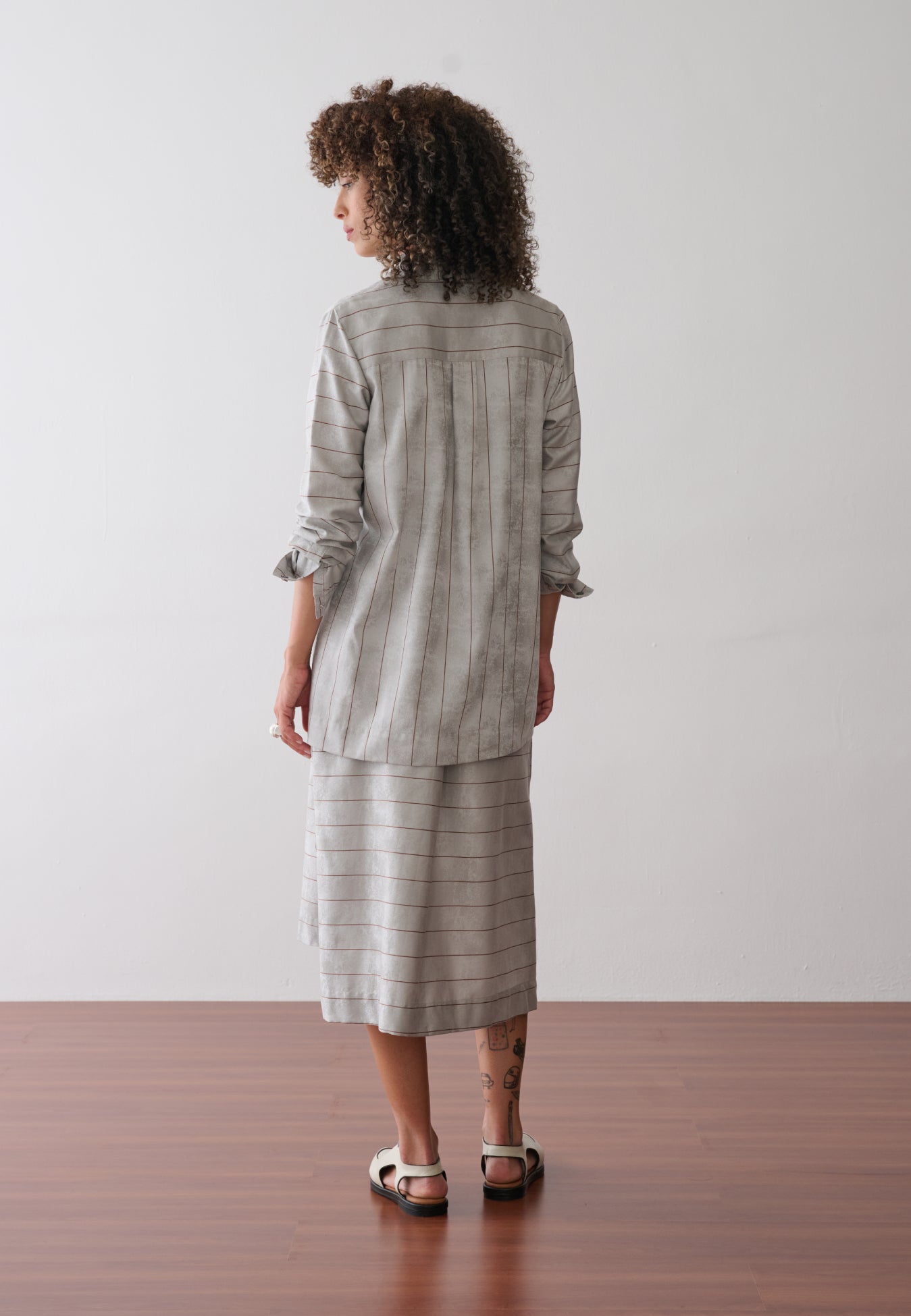 Modelo de costas usa um vestido midi com sobreposição integrada em cinza e listras marrons.