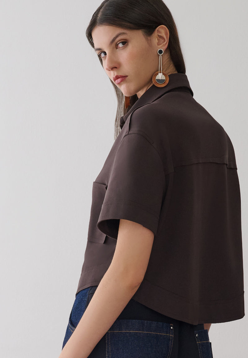 Modelo de costas veste uma camisa marrom de mangas curtas com recorte horizontal.