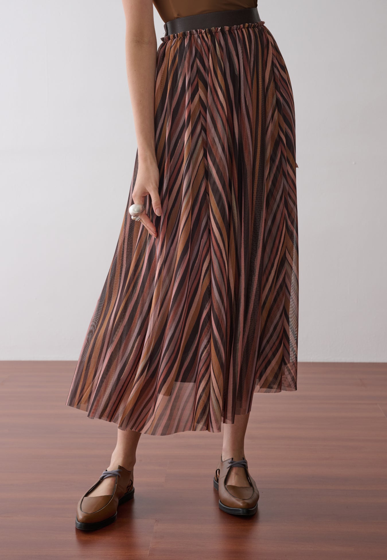 Modelo veste uma saia longa plissada em tule com estampa de listras multicoloridas.