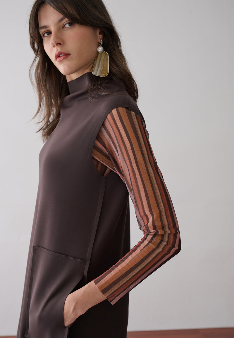 Modelo usa um vestido midi marrom de gola alta e bolsos frontais com  forro removível em tule de estampa listrada multicolorida.