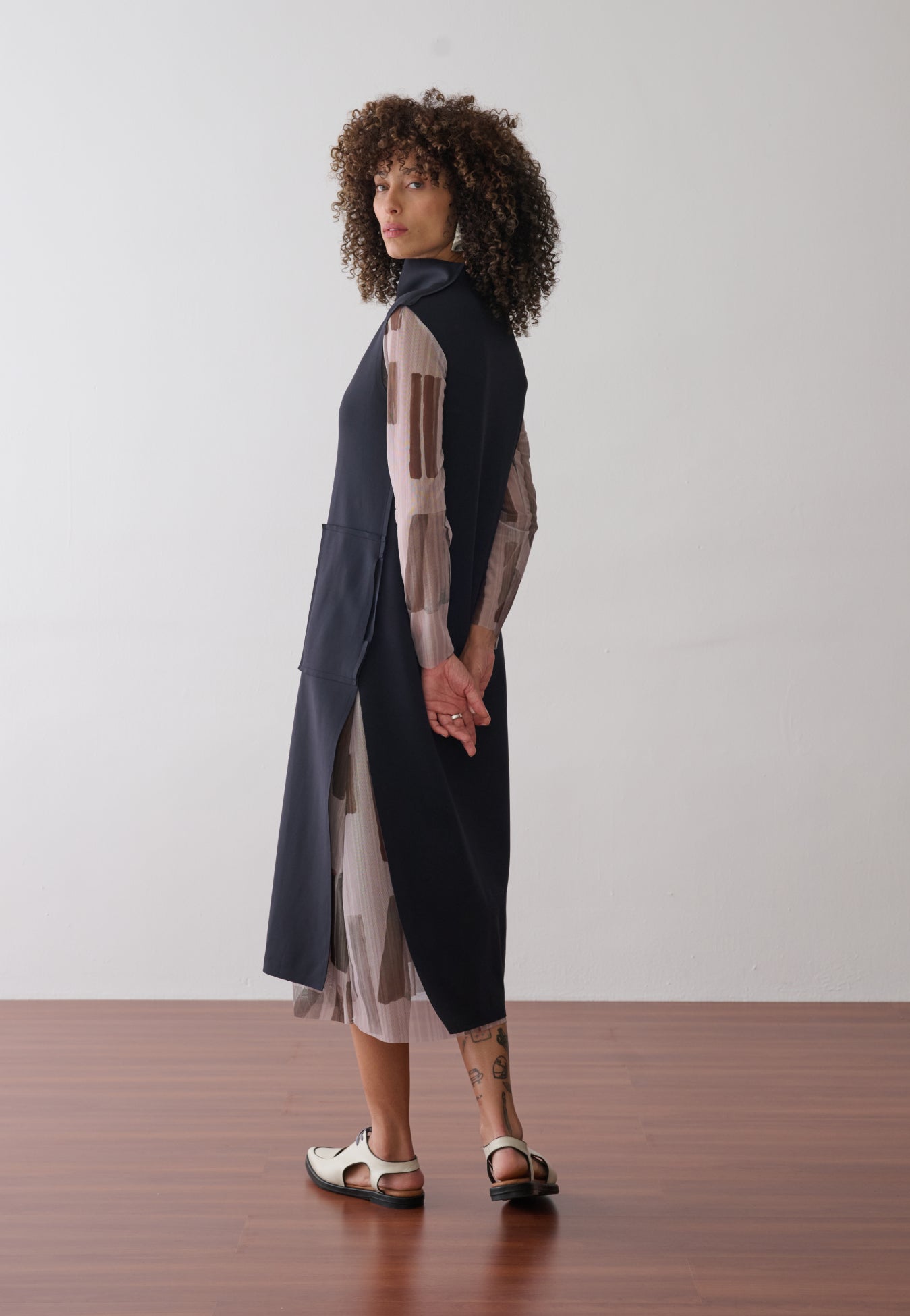 Modelo usa um vestido midi preto de gola alta e bolsos frontais com  forro removível em tule de estampa geométrica, combinados com sapatos off de bico fino.