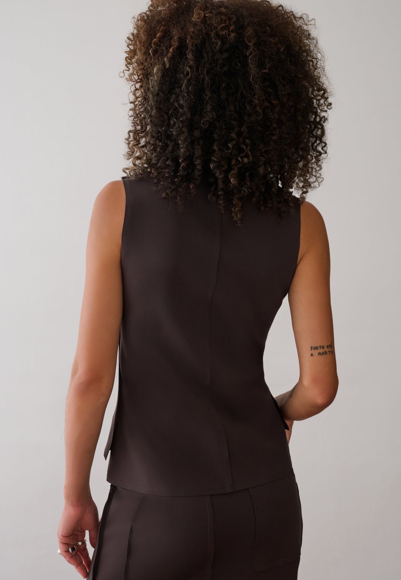 Modelo de costas veste uma blusa marrom sem mangas com recorte no meio.