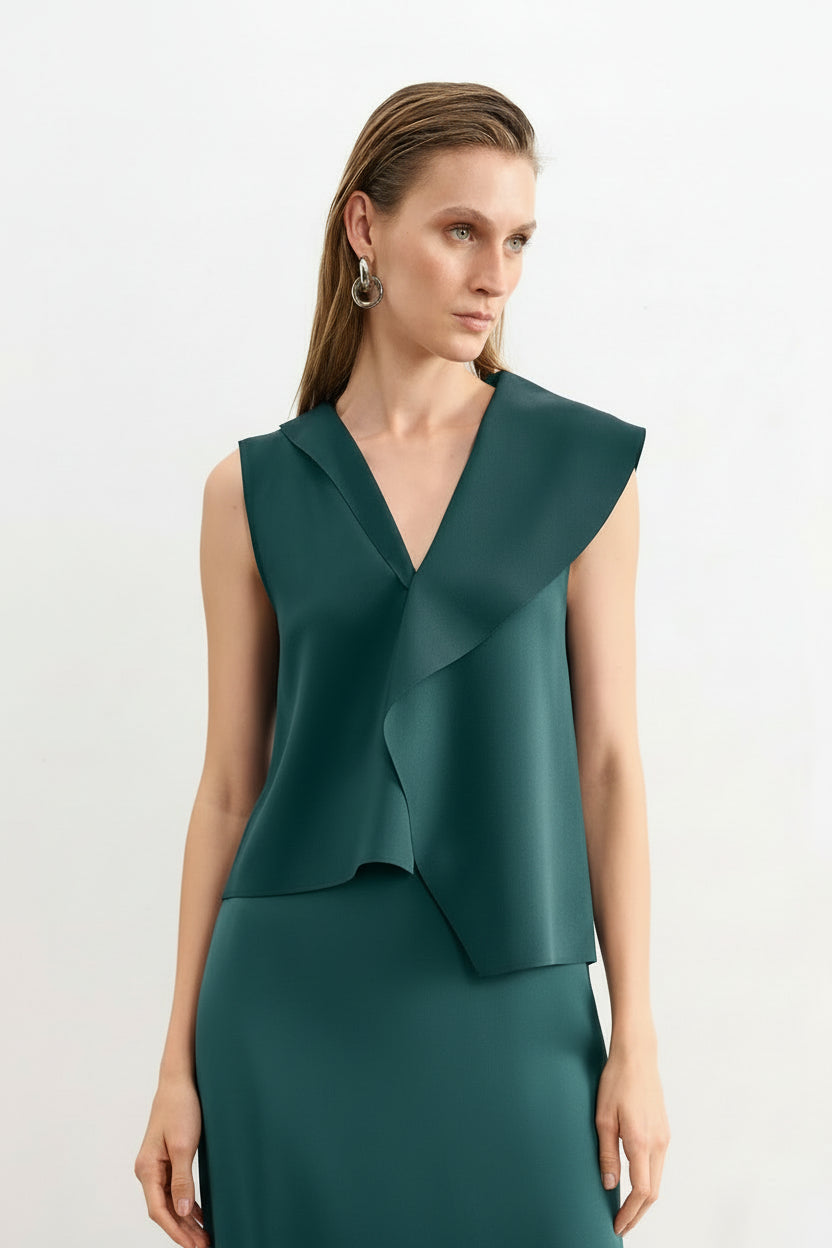 Modelo veste uma blusa verde petróleo sem mangas com lapelas assimétricas e gola em "V", combinada com saia reta da mesma cor.