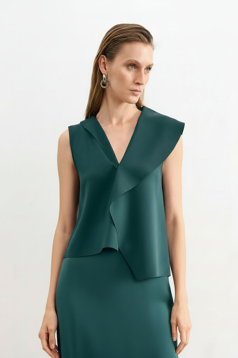 Modelo veste uma blusa verde petróleo sem mangas com lapelas assimétricas e gola em "V", combinada com saia reta da mesma cor.