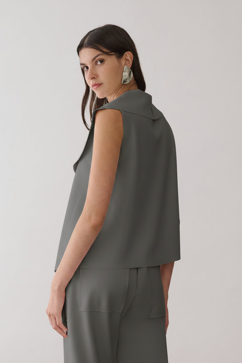 Modelo de costas veste uma blusa off-white sem mangas com gola aparente, combinada com calça reta da mesma cor com bolsos amplos.