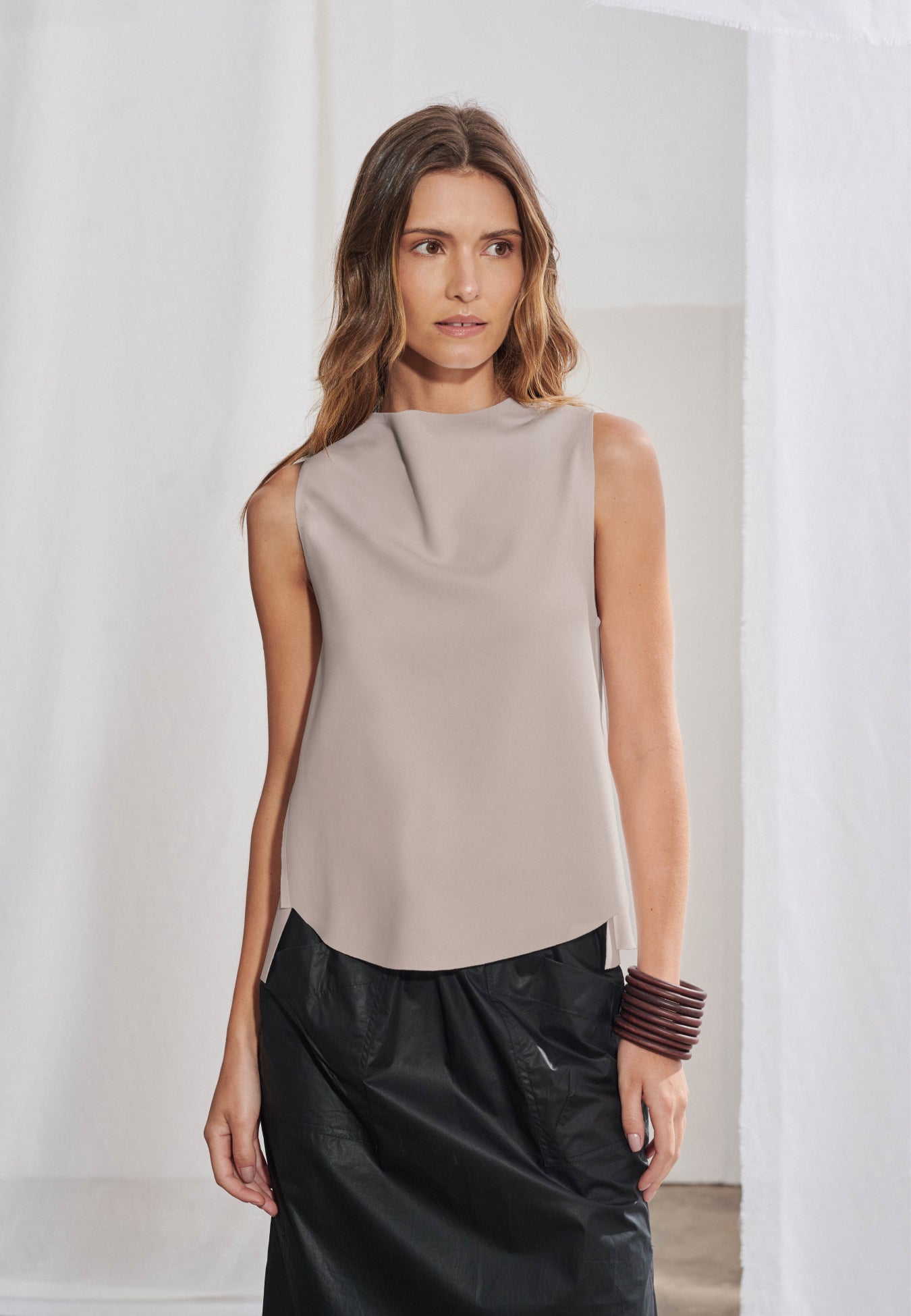 Blusa feminina sem mangas em malha tech. Gola alta transpassada com construção assimétrica degagê, modelagem evasê com barra frontal abaulada e acabamento a fio nas bordas. Aberturas sobrepostas visíveis nas laterais da frente.