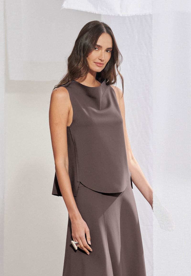 Blusa feminina sem mangas em malha tech. Gola alta transpassada com construção assimétrica degagê, modelagem evasê com barra frontal abaulada e acabamento a fio nas bordas. Aberturas sobrepostas visíveis nas laterais da frente.