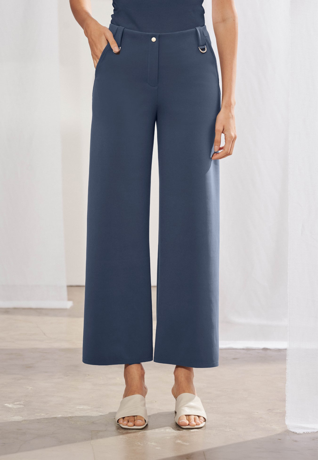Calça feminina wide leg reta com cós de passantes e duas meias-argolas metálicas aplicadas e bolsos faca laterais. As costas destacam dois bolsos chapados funcionais e recortes geométricos diagonais que se estendem até a barra. Peça com acabamento pespontado simples e caimento estruturado.