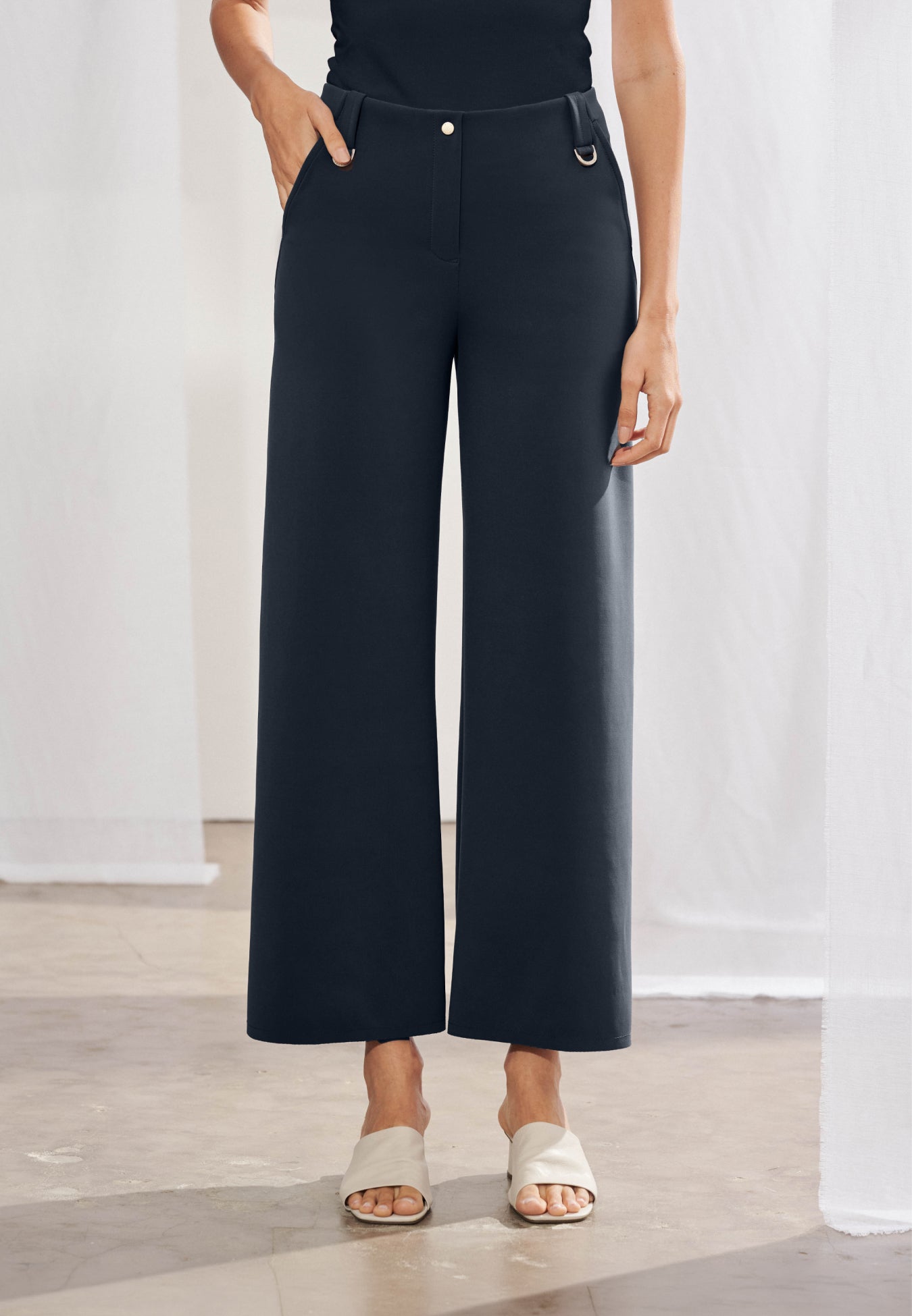 Calça feminina wide leg reta com cós de passantes e duas meias-argolas metálicas aplicadas e bolsos faca laterais. As costas destacam dois bolsos chapados funcionais e recortes geométricos diagonais que se estendem até a barra. Peça com acabamento pespontado simples e caimento estruturado.