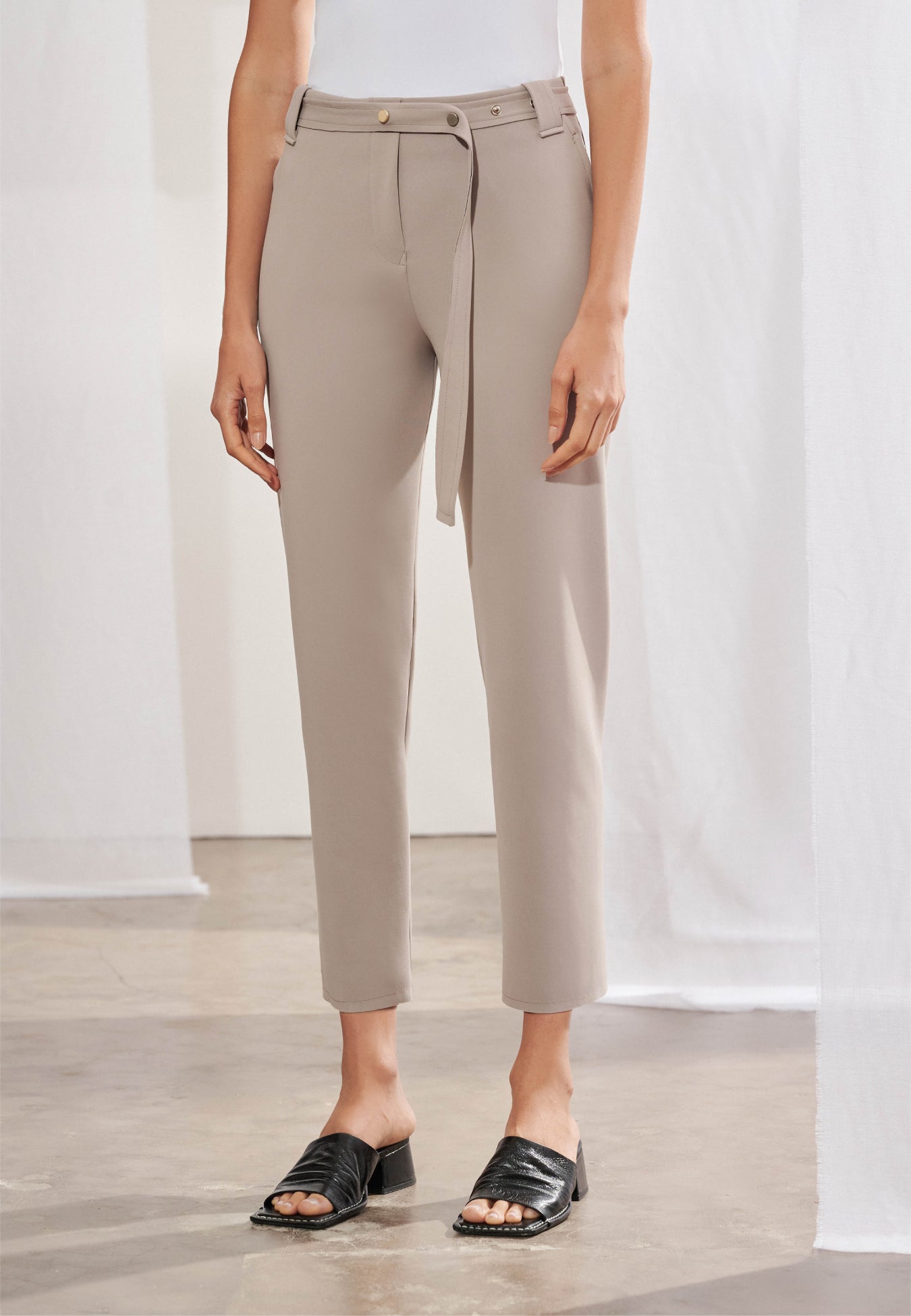Calça feminina de alfaiataria contemporânea em modelagem cigarrete slim. Na frente, apresenta cós com passantes, bolsos laterais tipo faca e cinto fino de mesmo material. Nas costas, destacam-se dois bolsos traseiros chapados com pontas, recortes anatômicos verticais que descem pelas pernas e terminam em pequenas fendas na barra.