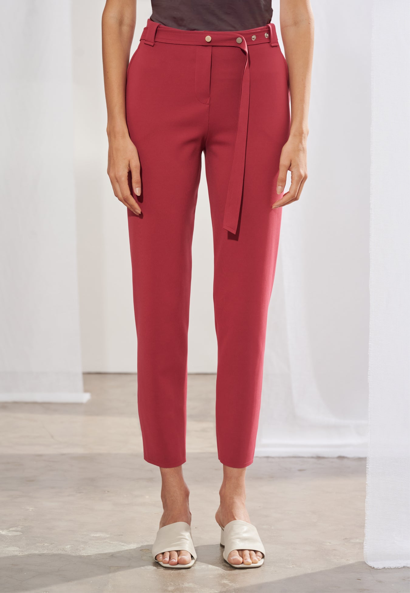 Calça feminina de alfaiataria contemporânea em modelagem cigarrete slim. Na frente, apresenta cós com passantes, bolsos laterais tipo faca e cinto fino de mesmo material. Nas costas, destacam-se dois bolsos traseiros chapados com pontas, recortes anatômicos verticais que descem pelas pernas e terminam em pequenas fendas na barra.
