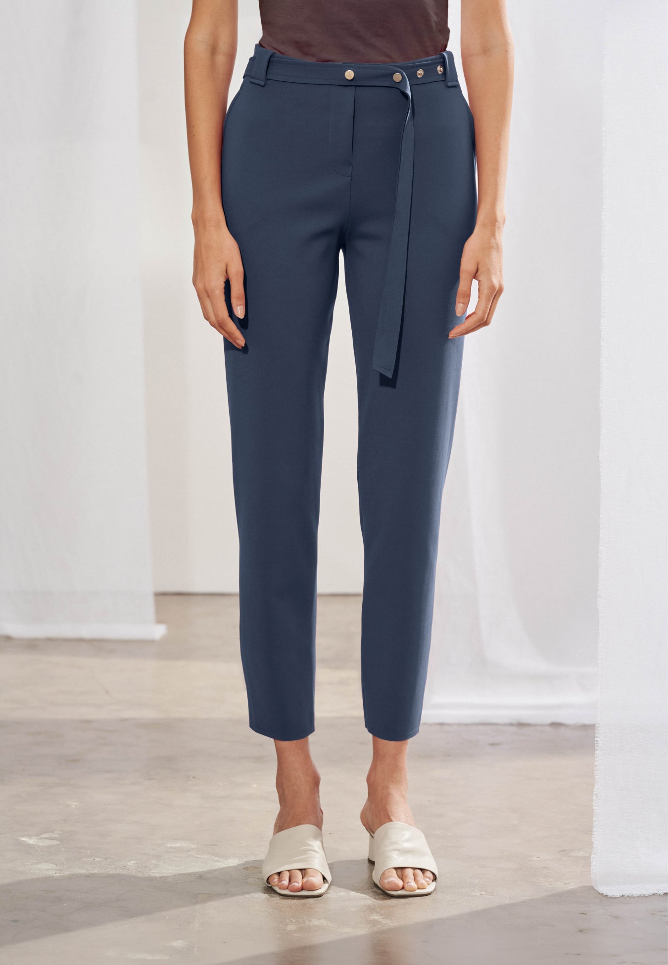 Calça feminina de alfaiataria contemporânea em modelagem cigarrete slim. Na frente, apresenta cós com passantes, bolsos laterais tipo faca e cinto fino de mesmo material. Nas costas, destacam-se dois bolsos traseiros chapados com pontas, recortes anatômicos verticais que descem pelas pernas e terminam em pequenas fendas na barra.