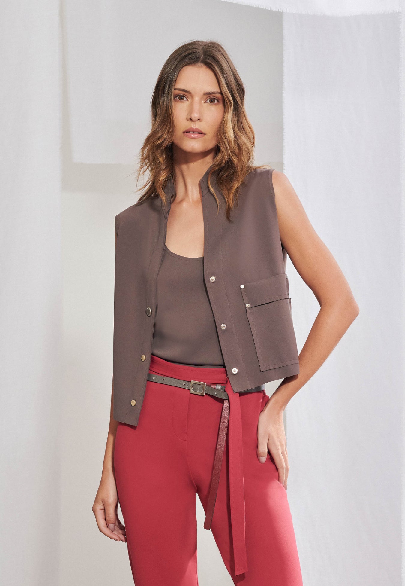 Colete feminino com modelagem reta estruturada em malha Tech. Possui gola padre com decote V, fechamento frontal por três botões de pressão prateados e bolso chapado funcional do lado esquerdo com lapela e detalhe de rebites metálicos. 