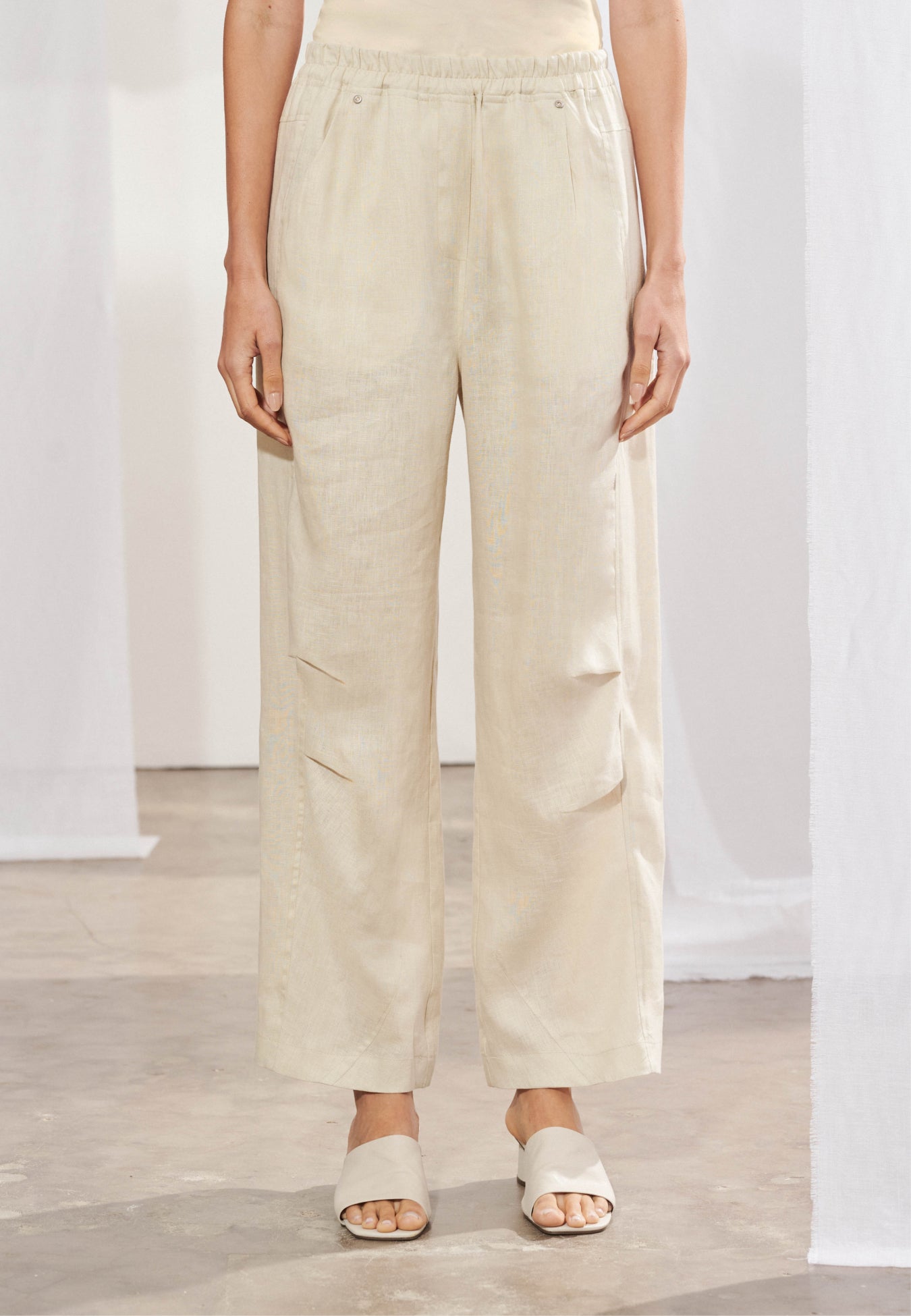 Calça reta longa em linho natural com cós elástico e cordão frontal. Passantes para cinto, bolsos frontais e dois bolsos traseiros chapados. Vista frontal.