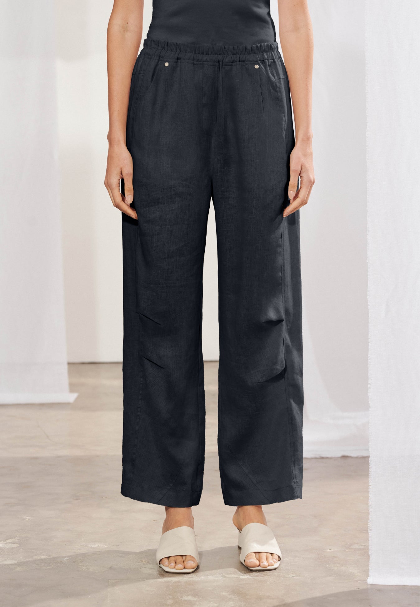 Calça reta longa em linho natural com cós elástico e cordão frontal. Passantes para cinto, bolsos frontais e dois bolsos traseiros chapados. Vista frontal.