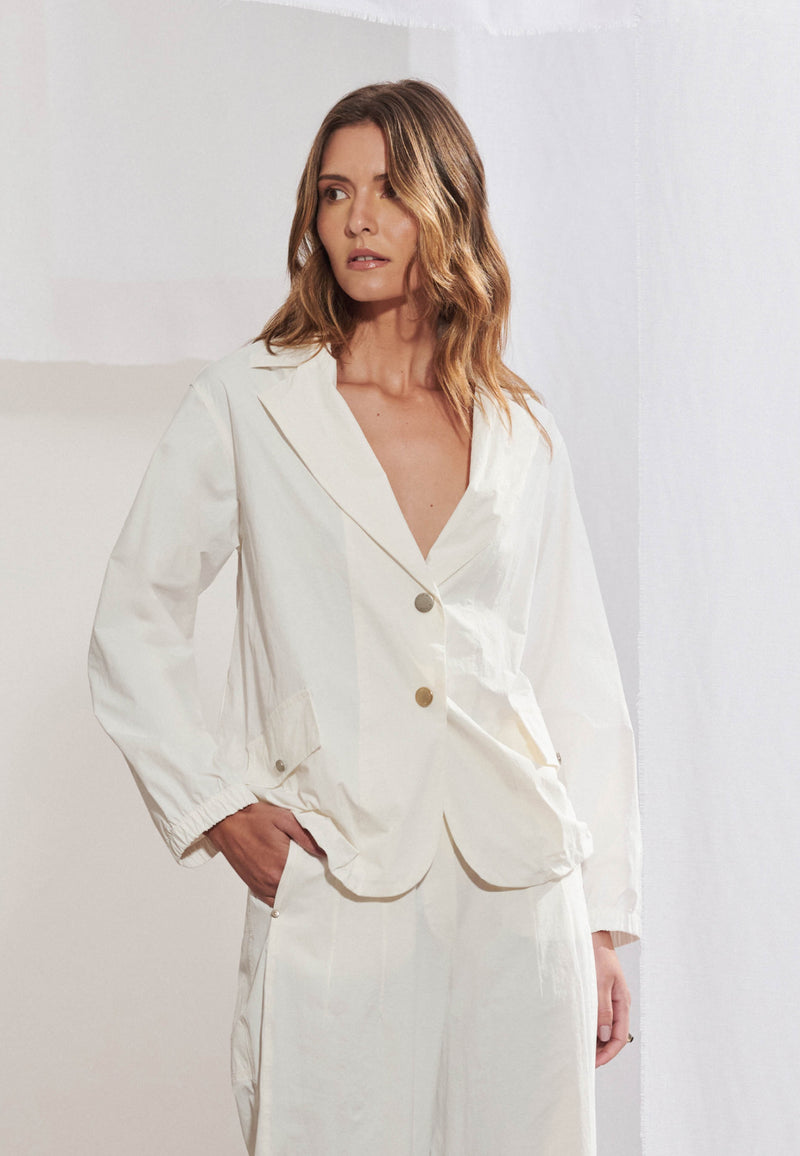 Blazer longo feminino em tecido tech de modelagem ampla. Gola alfaiataria com lapela larga, fechamento frontal por botões, bolsos com aba e mangas de comprimento 7/8. Vista frontal sobre fundo neutro.