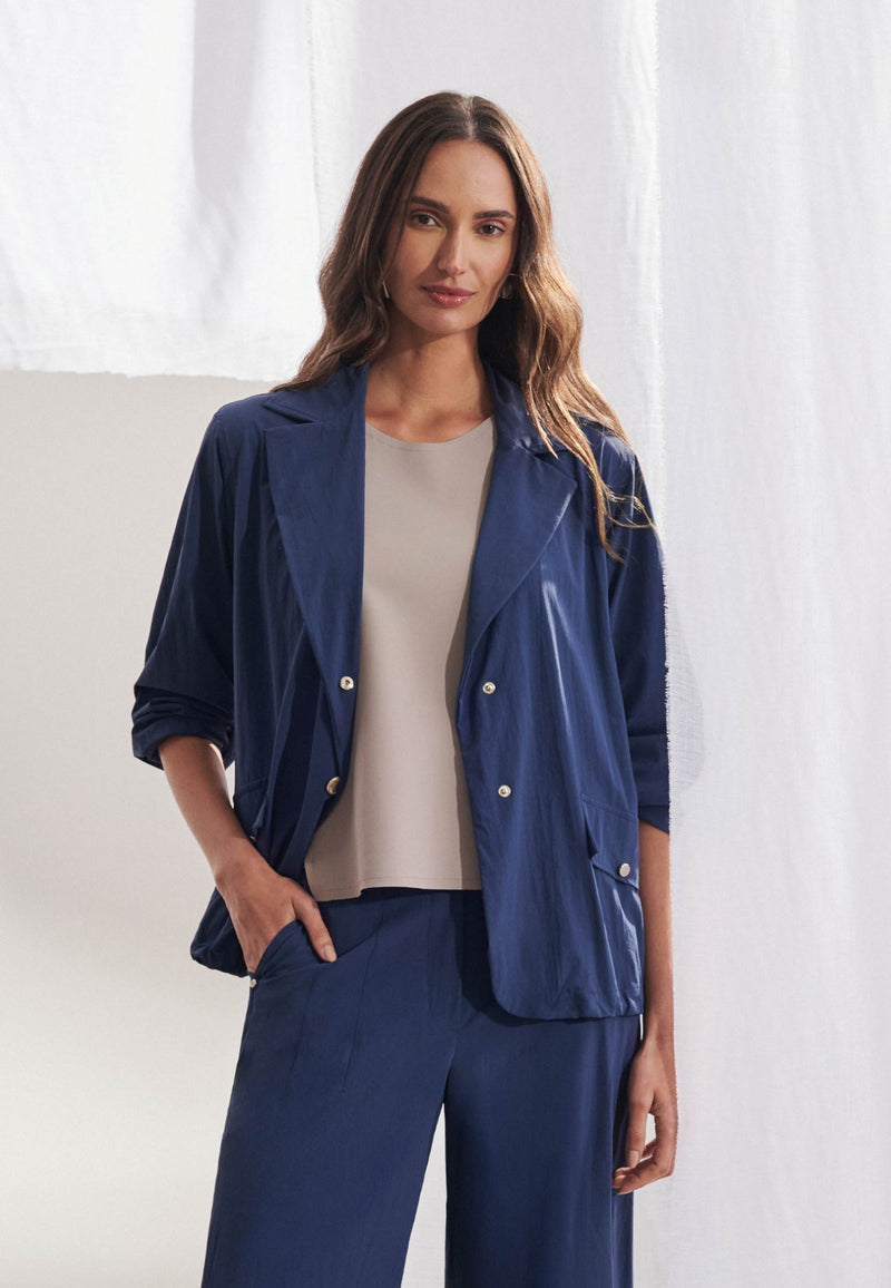 Blazer longo feminino em tecido tech de modelagem ampla. Gola alfaiataria com lapela larga, fechamento frontal por botões, bolsos com aba e mangas de comprimento 7/8. Vista frontal sobre fundo neutro.