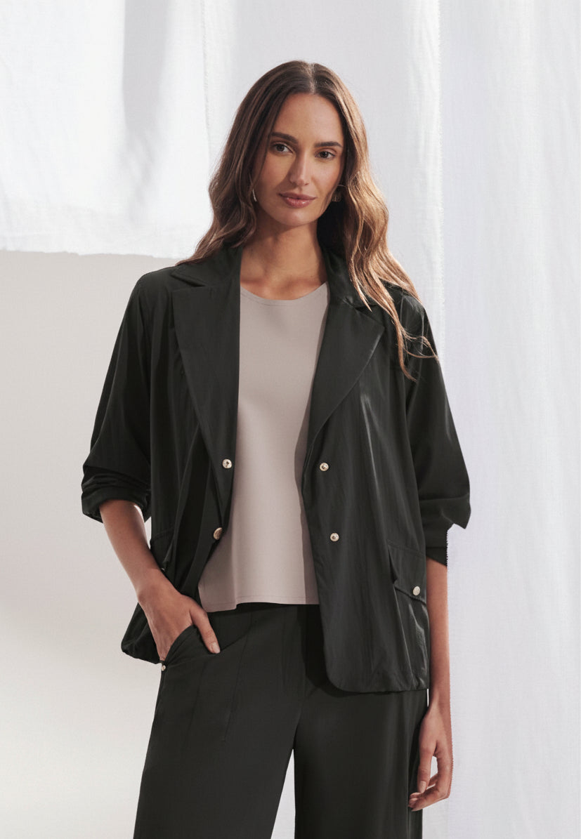 Blazer longo feminino em tecido tech de modelagem ampla. Gola alfaiataria com lapela larga, fechamento frontal por botões, bolsos com aba e mangas de comprimento 7/8. Vista frontal sobre fundo neutro.