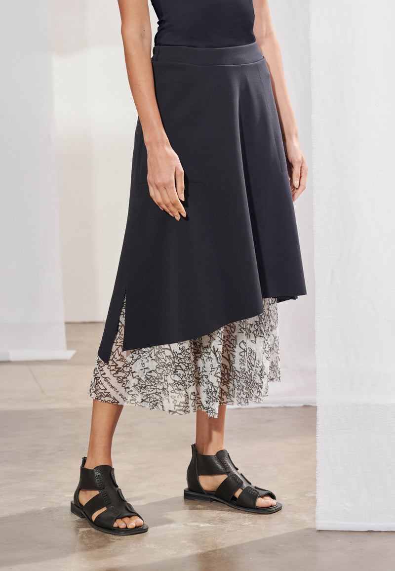 Saia midi feminina com modelagem evasê e sobreposição de duas camadas. A camada superior é feita em malha Tech, barra assimétrica diagonal e fendas laterais que revelam bolsos embutidos. A camada inferior é feita em tule fluido com estampa exclusiva em tons neutros, com comprimento que termina na altura da panturrilha.