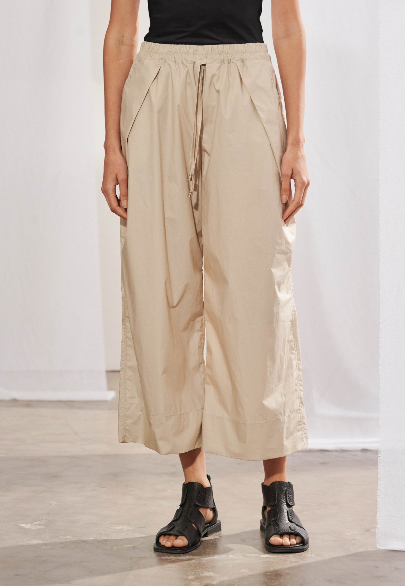 Calça 100% algodão com acabamento encerado estruturado. A peça possui modelagem ampla, comprimento midi na altura da panturrilha, cós elástico com cordão para regulação e amarração e pregas diagonais geométricas.
