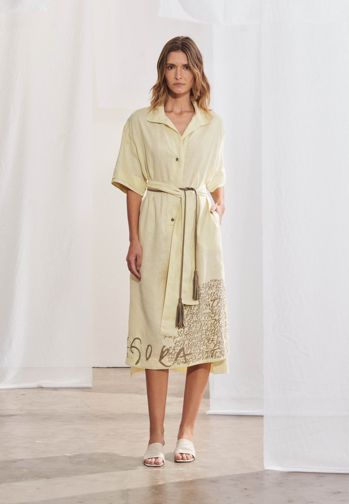 Vestido chemise midi em malha com gola clássica e decote V suave, fechamento frontal por botões e mangas curtas com ombros levemente deslocados. Faixa de amarração na cintura. Fendas laterais e barra levemente assimétrica com estampa localizada de grafismos.