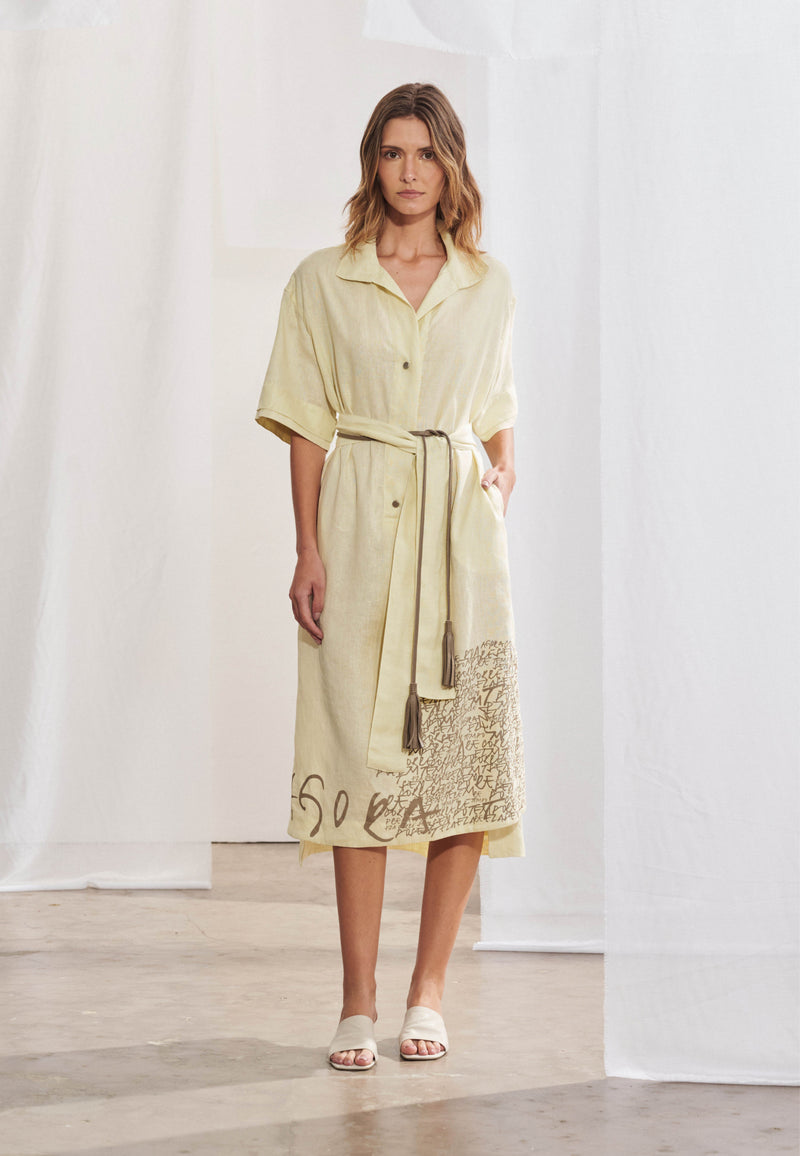 Vestido chemise midi em malha com gola clássica e decote V suave, fechamento frontal por botões e mangas curtas com ombros levemente deslocados. Faixa de amarração na cintura. Fendas laterais e barra levemente assimétrica com estampa localizada de grafismos.