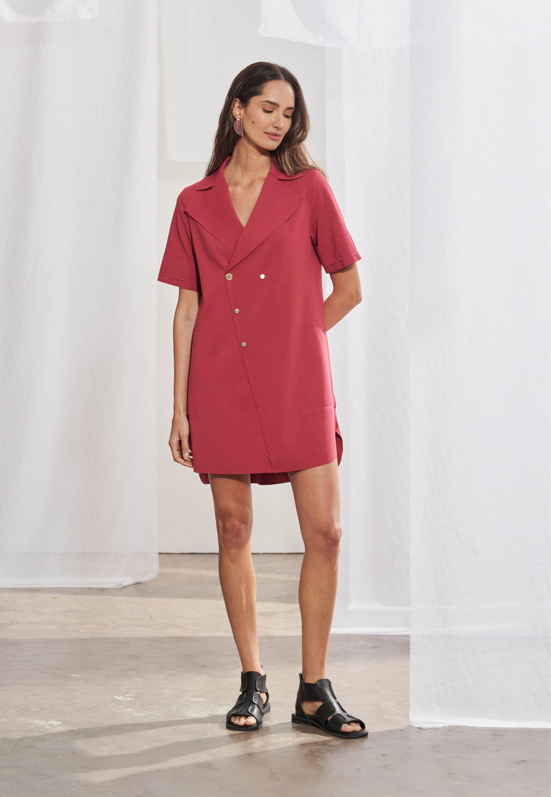 Vestido feminino estilo chemise em malha tech de modelagem ampla. Lapela chanfrada, decote V transpassado, mangas curtas com detalhe sobreposto, bolsos laterais chapados e barra assimétrica com fendas curvilíneas. Vista frontal e lateral.