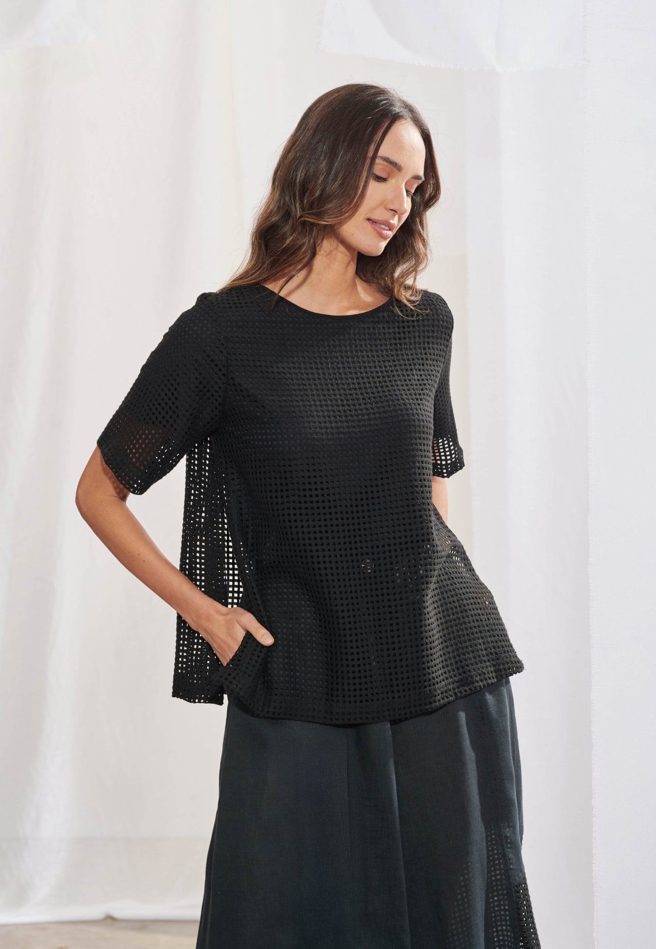 Blusa feminina ampla em malha telada com decote canoa acabado em viés. Mangas curtas com transparência visível na trama. Fendas laterais proeminentes na barra. Vista frontal mostrando a textura da tela no corpo e mangas.