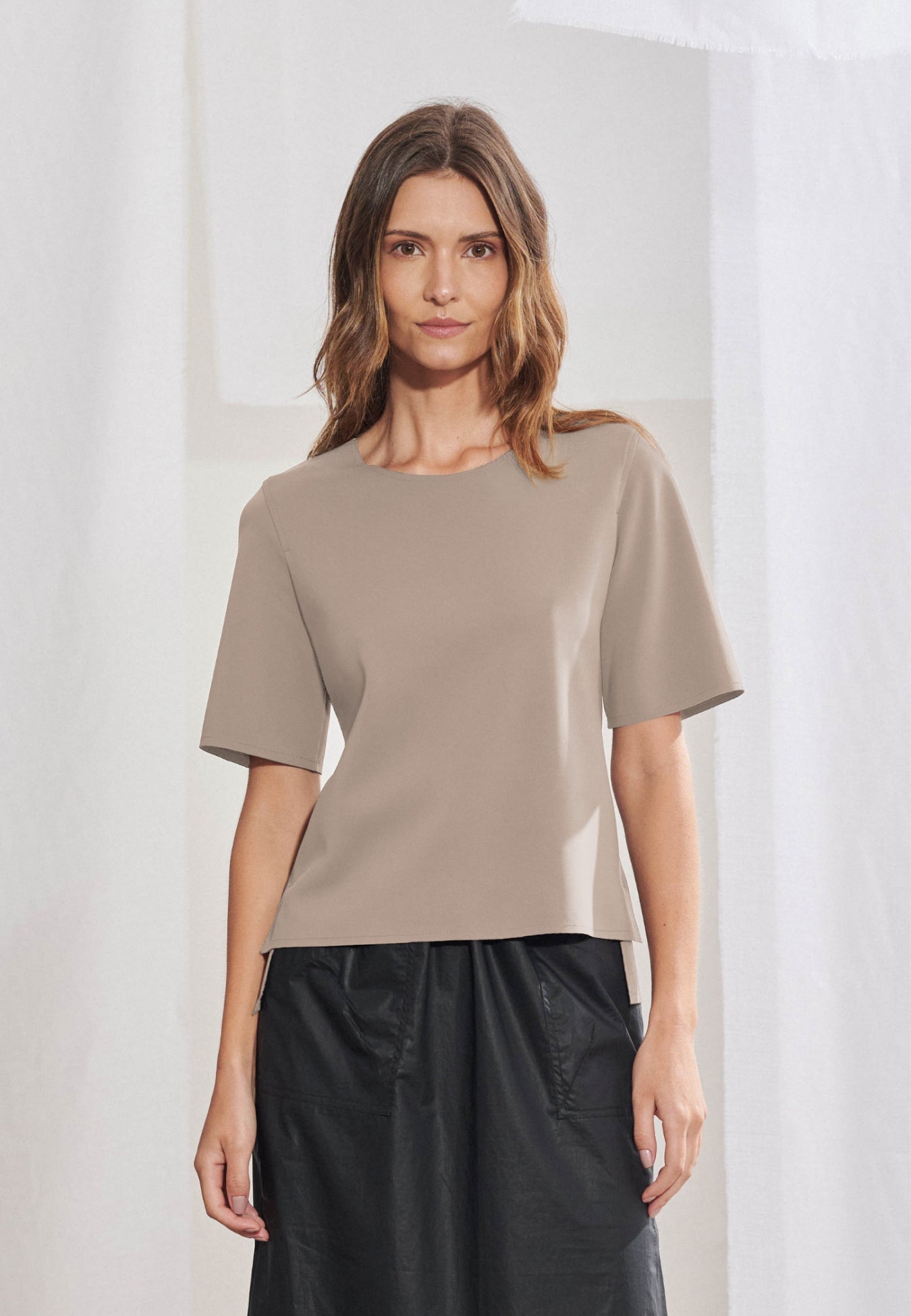 Blusa feminina de manga curta em malha tech de alta gramatura. Decote arredondado limpo, mangas curtas, barra assimétrica com fendas laterais e costas levemente alongadas. Acabamento a fio. Vista frontal e posterior.