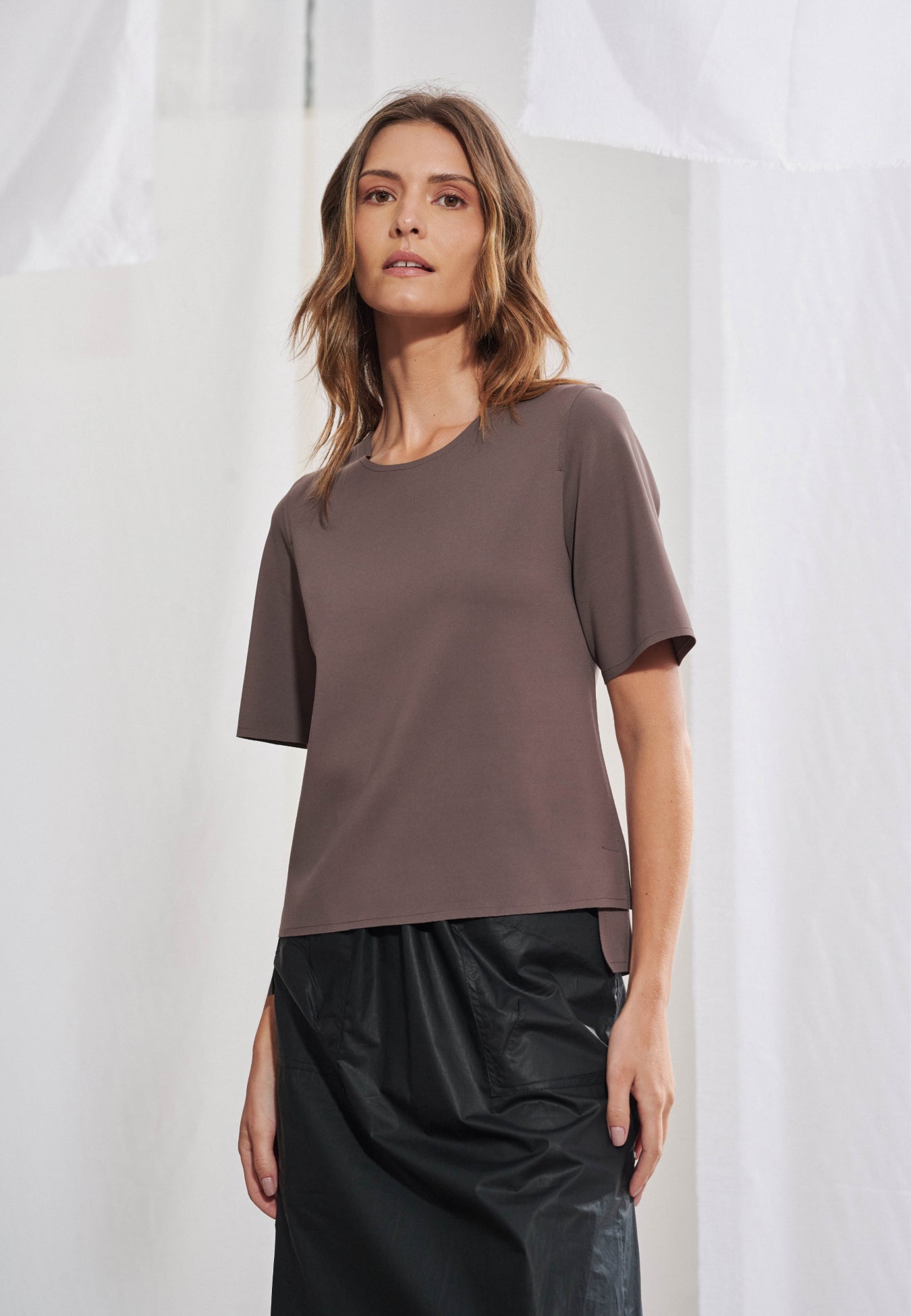 Blusa feminina de manga curta em malha tech de alta gramatura. Decote arredondado limpo, mangas curtas, barra assimétrica com fendas laterais e costas levemente alongadas. Acabamento a fio. Vista frontal e posterior.