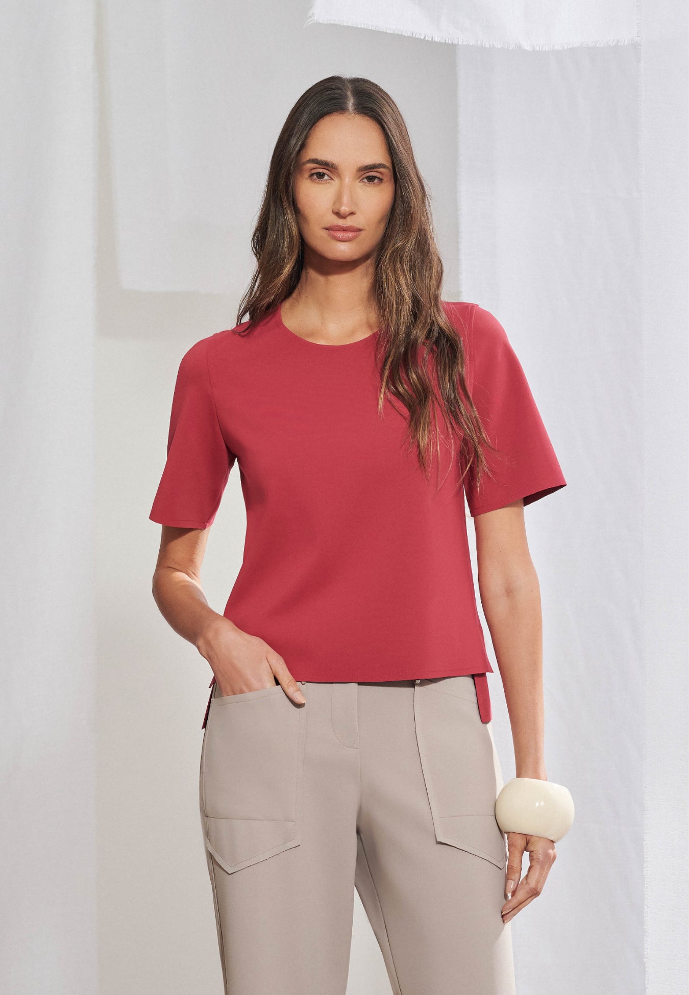 Blusa feminina de manga curta em malha tech de alta gramatura. Decote arredondado limpo, mangas curtas, barra assimétrica com fendas laterais e costas levemente alongadas. Acabamento a fio. Vista frontal e posterior.