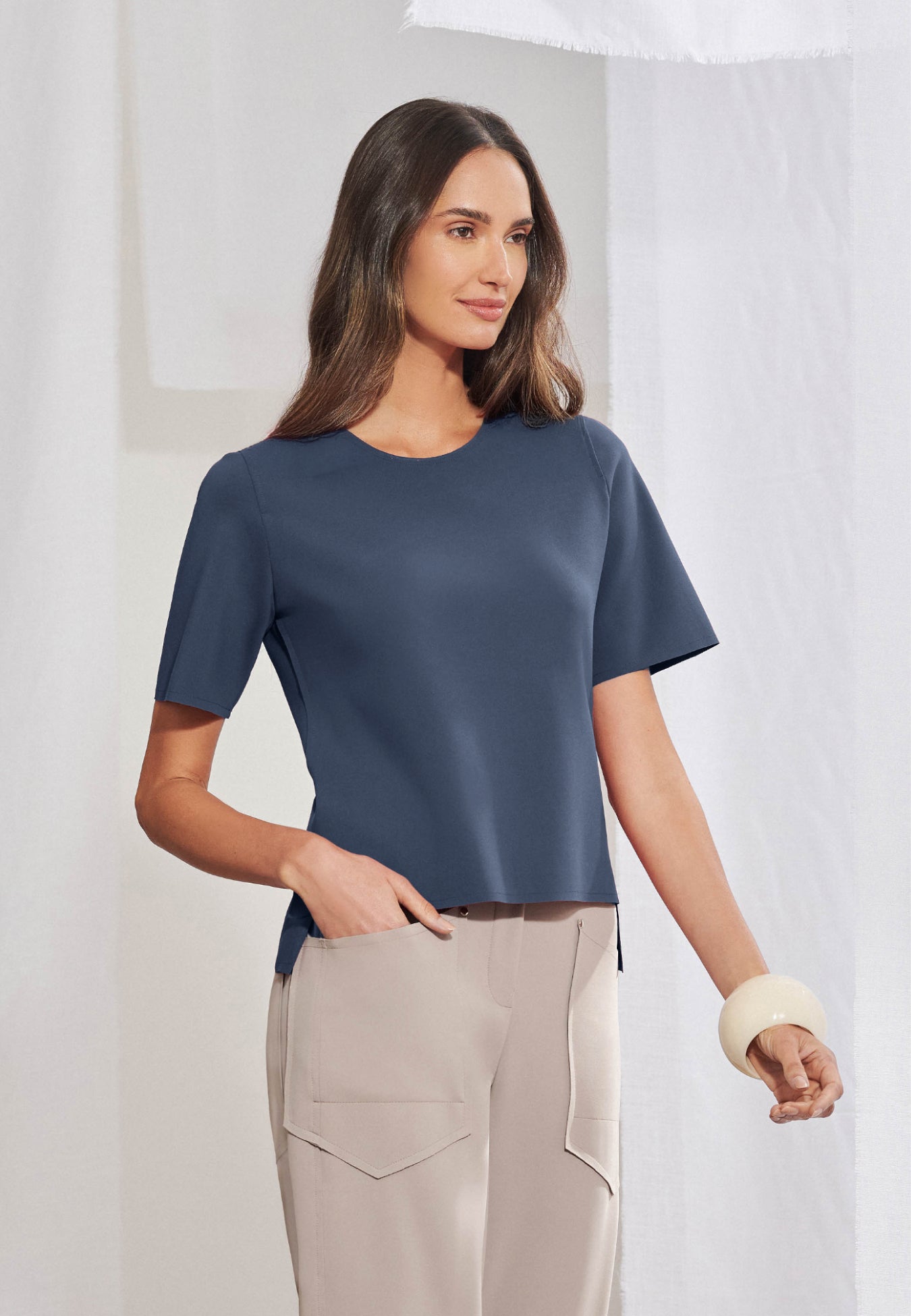 Blusa feminina de manga curta em malha tech de alta gramatura. Decote arredondado limpo, mangas curtas, barra assimétrica com fendas laterais e costas levemente alongadas. Acabamento a fio. Vista frontal e posterior.