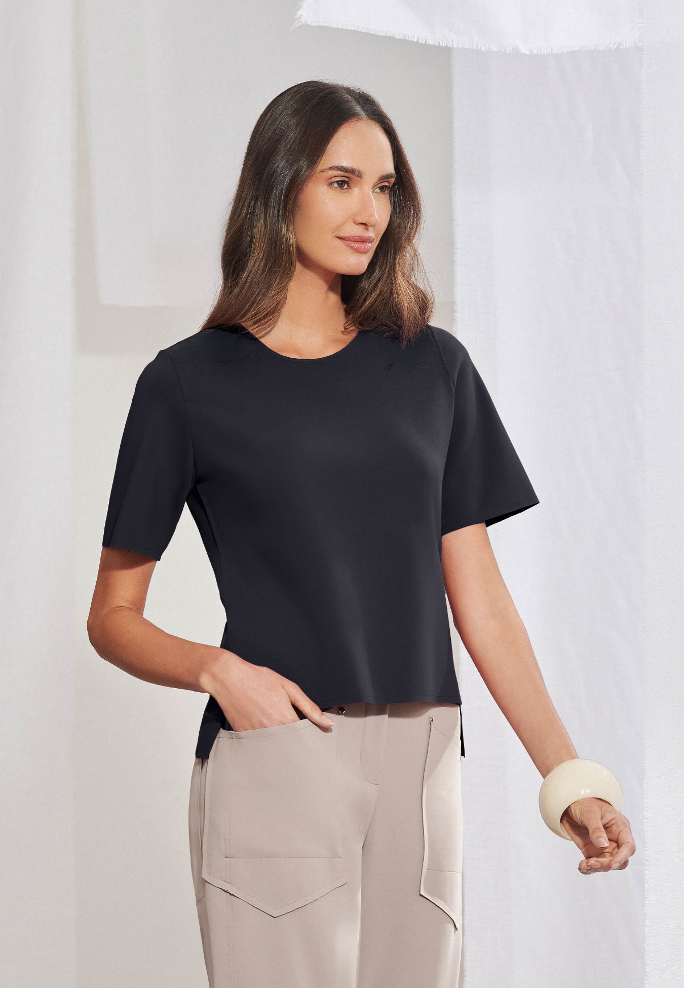 Blusa feminina de manga curta em malha tech de alta gramatura. Decote arredondado limpo, mangas curtas, barra assimétrica com fendas laterais e costas levemente alongadas. Acabamento a fio. Vista frontal e posterior.