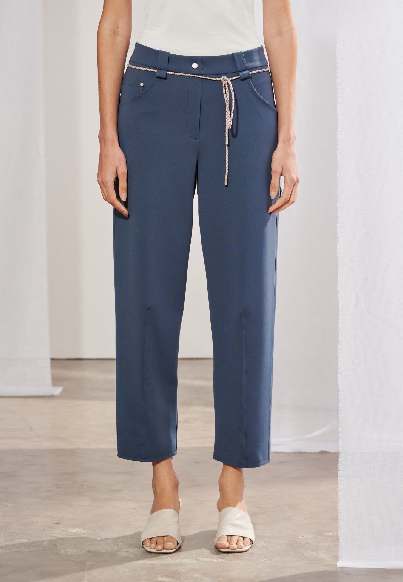 Calça de alfaiataria feminina com modelagem reta e leve afunilamento na barra. Cós com passantes e elástico posterior. Nervuras verticais centralizadas na frente das pernas. Cinto em cordão fino com ponteiras metálicas. Vista frontal e posterior.